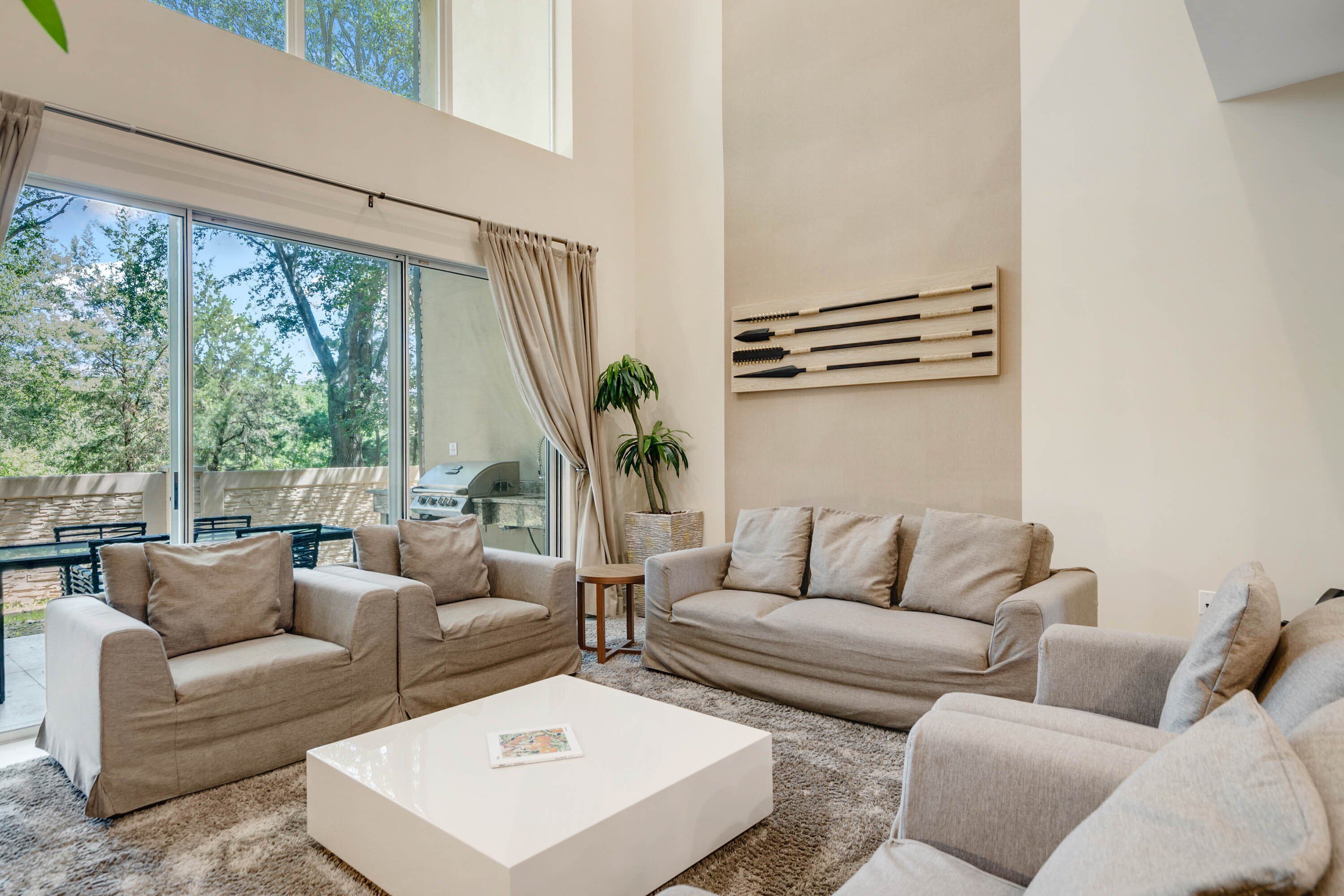 Ein geräumiges Wohnzimmer mit großem Fenster, beigefarbenen Sofas, einem weißen Couchtisch und einem an der Wand befestigten Holzbild.