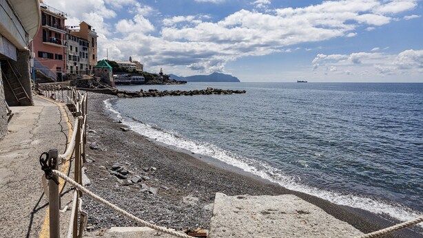 Uma paisagem costeira com uma praia rochosa, uma passarela de madeira e edifícios na orla.