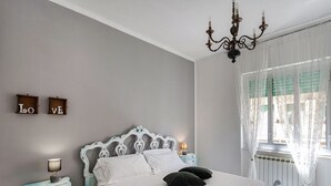 A neatly arranged bedroom with a bed, bedside tables, a chandelier, and a window with curtains.