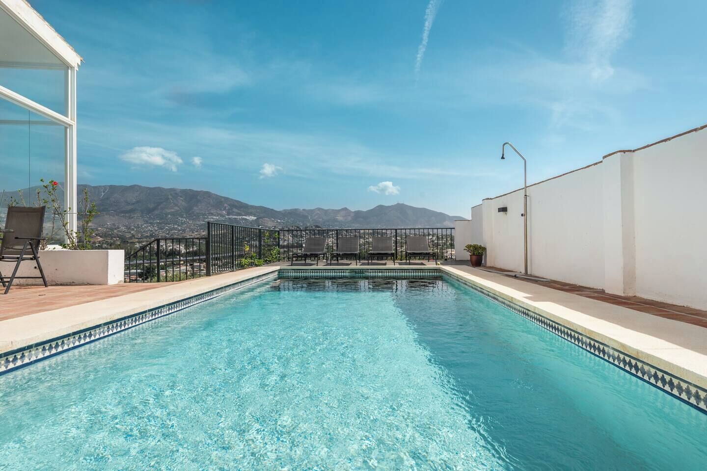 A rectangular swimming pool with clear blue water, surrounded by a white wall and a metal fence.