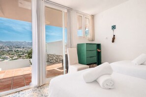 A hotel room with a balcony, a green cabinet, a bed with white linens, and a view of a cityscape.