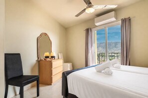 A hotel room with a bed, a chair, a dresser, a mirror, and a window with a view of the mountains. - Casa Kodak - Cerros de Aguila (Las Lagunas de Mijas)