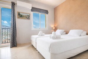 Quarto de hotel com cama, duas almofadas, janela com vista, pintura na parede e cortina estampada.