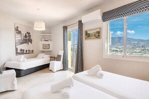 Ein Hotelzimmer mit zwei Betten, einem großen Fenster mit Blick auf die Stadt, einer Deckenleuchte und einem Gemälde an der Wand.