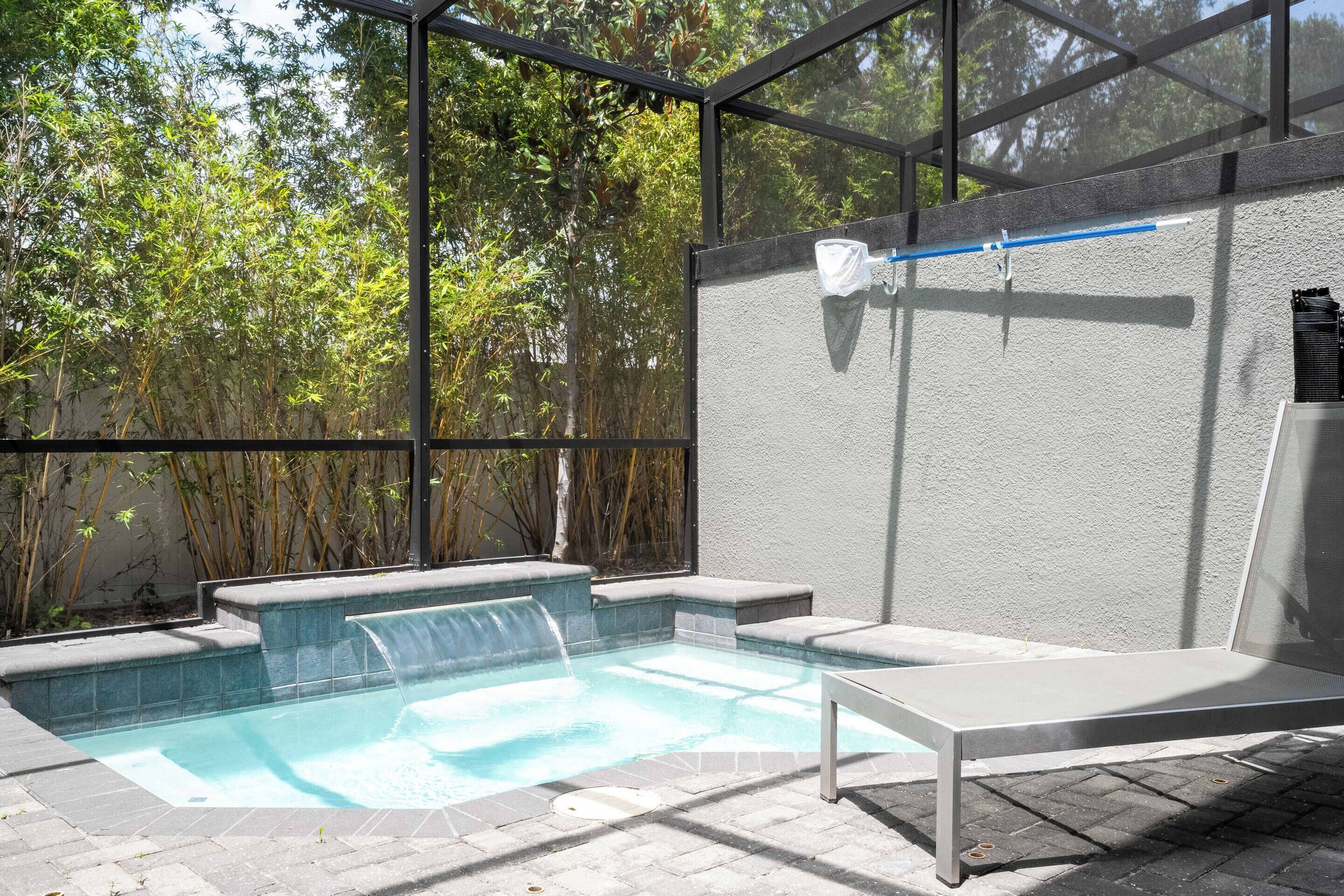 A pool area with a waterfall feature, surrounded by a glass enclosure and bamboo plants.