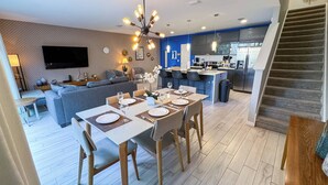 Un salon moderne comprenant un coin repas, une cuisine et un escalier.