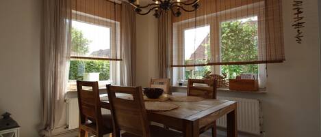 A dining room with a wooden table, chairs, a chandelier, and large windows with curtains.