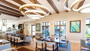 A spacious dining area with multiple tables and chairs, large windows, and a modern ceiling design.