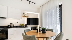Una cocina moderna con armarios blancos, encimera negra y una mesa de comedor redonda de madera con cuatro sillas grises.