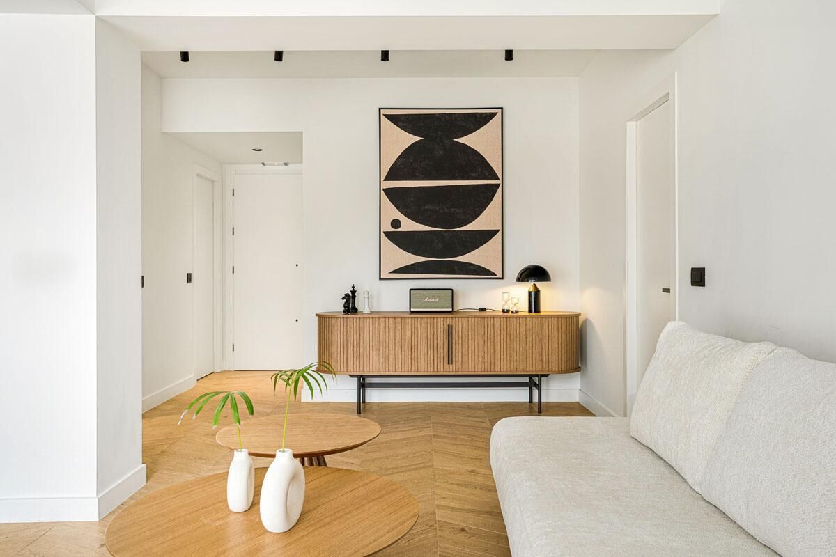 A modern living room with a wooden floor, a round coffee table, a beige sofa, a wooden cabinet, and a large abstract painting on the wall.