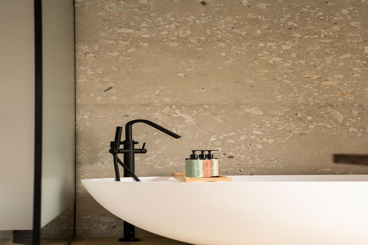 Une salle de bain avec un lavabo blanc, un robinet noir et un mur à texture.