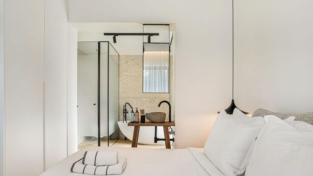 Ein modernes Schlafzimmer mit einem großen Bett, einem Nachttisch aus Holz mit einem Waschbecken und einem Spiegel über dem Waschbecken.