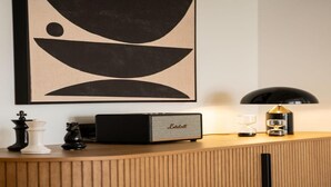 Ein Holzschrank mit einem Lautsprecher obenauf, Schachfiguren und einem gerahmten abstrakten Kunstwerk.