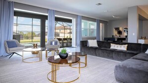 A modern living room with a grey sofa, two armchairs, and a coffee table. There is a balcony with a view of the outside. - Breathtaking Home Private Pool Game Room 1725 (Kissimmee)