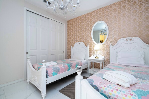 Une chambre avec deux lits, une porte blanche, un lustre et un miroir.