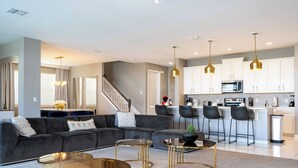 A modern living room with a grey sofa, a glass coffee table, and a kitchen area with white cabinets and a microwave. - Breathtaking Home Private Pool Game Room 1725 (Kissimmee)