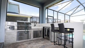 A modern kitchen with a built-in grill, stainless steel appliances, and a bar area with seating. - Breathtaking Home Private Pool Game Room 1725 (Kissimmee)