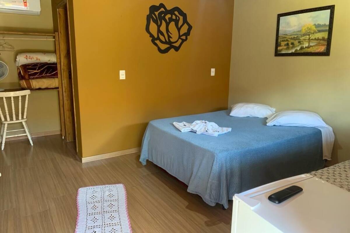 Une chambre à coucher comprenant un lit, une chaise, une petite table, un climatiseur fixé au mur et un tableau.