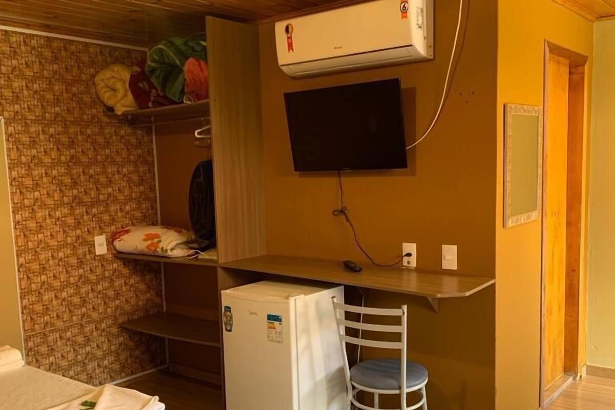 Une chambre de taille modeste, équipée de deux lits, d’un petit bureau avec une chaise, d’une télévision et d’un réfrigérateur.