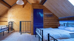 A wooden cabin with a sloped ceiling, a bed with white bedding, a blue door, and a hanging light fixture. - Vacation home in the Ouche Valley Situated between Dijon and Beaune.  (La Bussière-sur-Ouche)