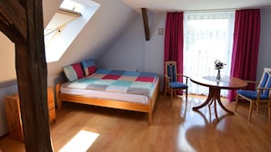 Une chambre avec un lit en bois, un puits de lumière, une table à manger avec des chaises et une fenêtre avec des rideaux.