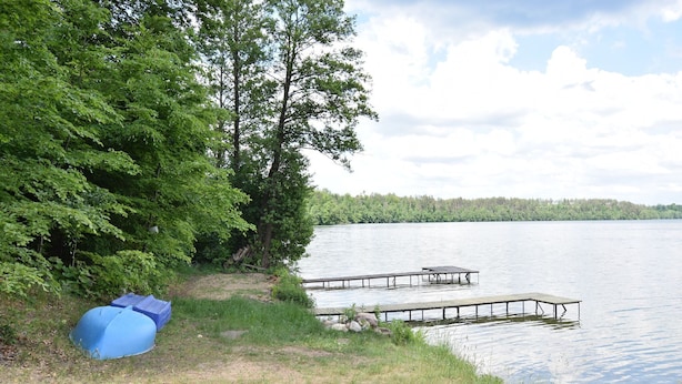 Un terrain de camping au bord du lac, équipé d’une tente, d’un quai et bordé d’une forêt.