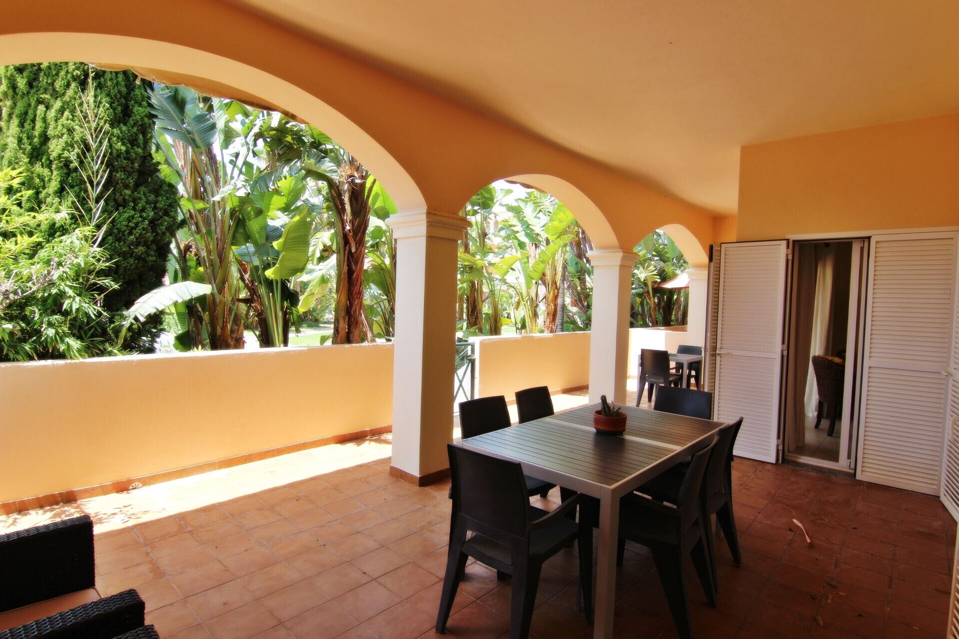 An outdoor patio with a table and chairs, surrounded by arches and lush greenery.