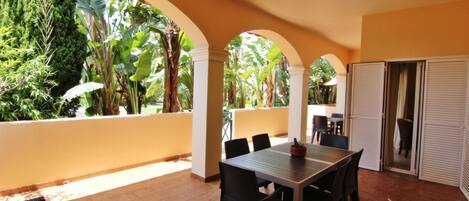 An outdoor patio with a table and chairs, surrounded by arches and lush greenery.