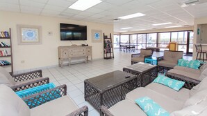 A spacious living area with a large flat-screen TV, comfortable seating, and a view through large windows.