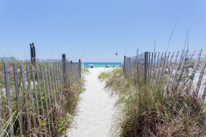 Un sentier de sable bordé de clôtures en bois qui mène  à l’océan.