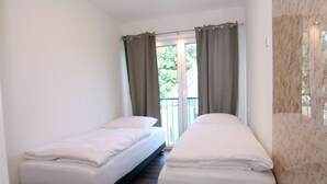 A room with two single beds, a window with curtains, and a view of greenery outside.