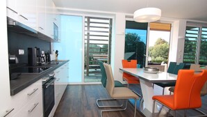 A modern kitchen with a dining area, featuring a large window, a built-in oven, and a dining table with orange chairs.