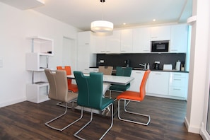 Une cuisine moderne avec des meubles blancs, un micro-ondes noir et un coin repas comprenant une table et des chaises.