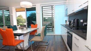 A modern kitchen with a large island, white cabinets, and a dining area with orange chairs.