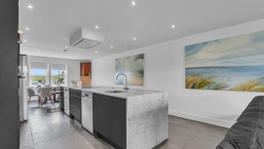 Een moderne keuken met een centraal eiland, een zithoek met stoelen en een groot schilderij aan de muur.