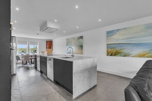 A modern kitchen with a central island, a dining area with chairs, and a large painting on the wall. - The Duke - North East Escapes (Bamburgh)