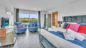 Een moderne hotelkamer met een groot bed, twee fauteuils, een televisie en uitzicht op de omgeving.