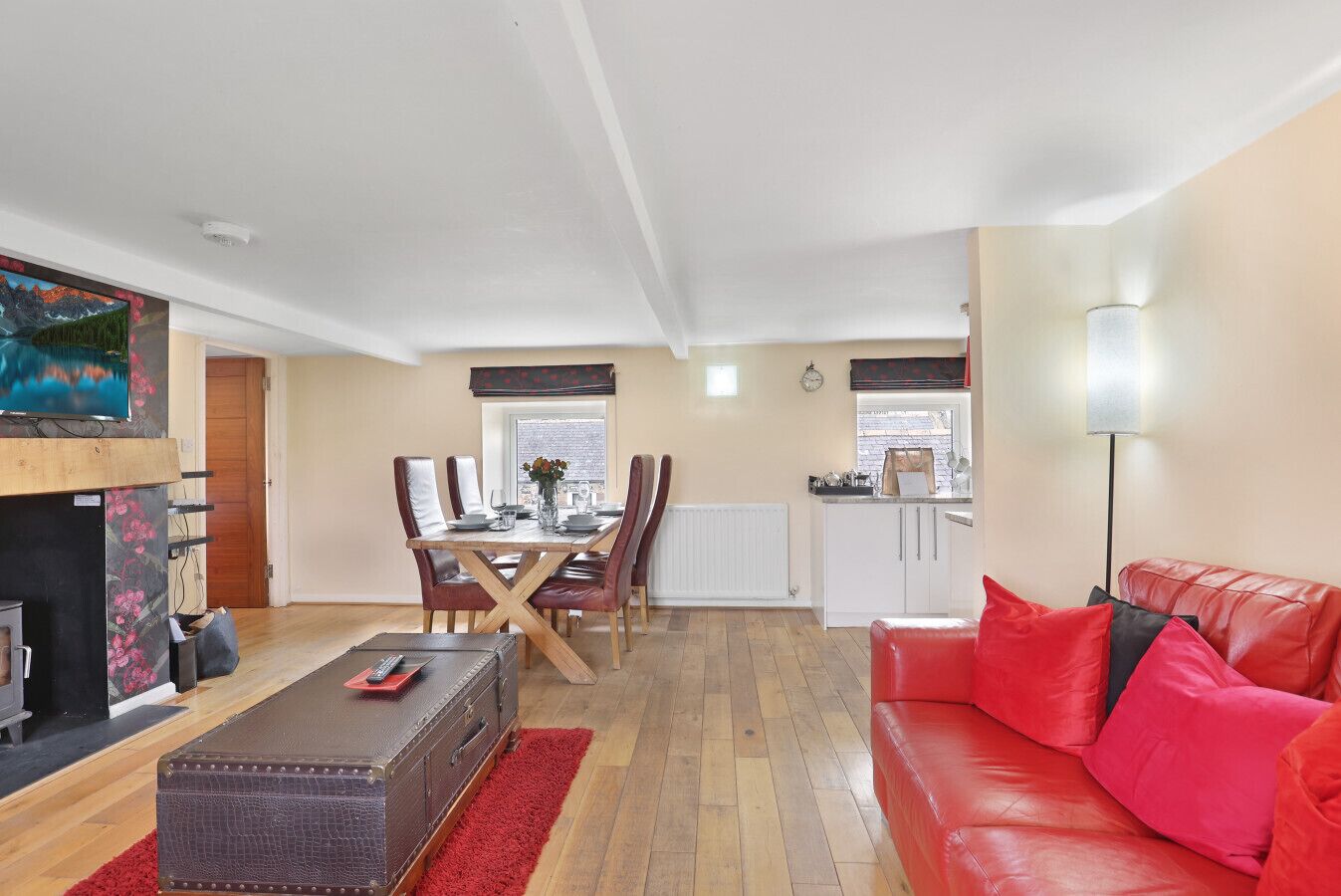 A living room with a red sofa, a dining area with a table and chairs, a kitchen with white cabinets, and a fireplace.