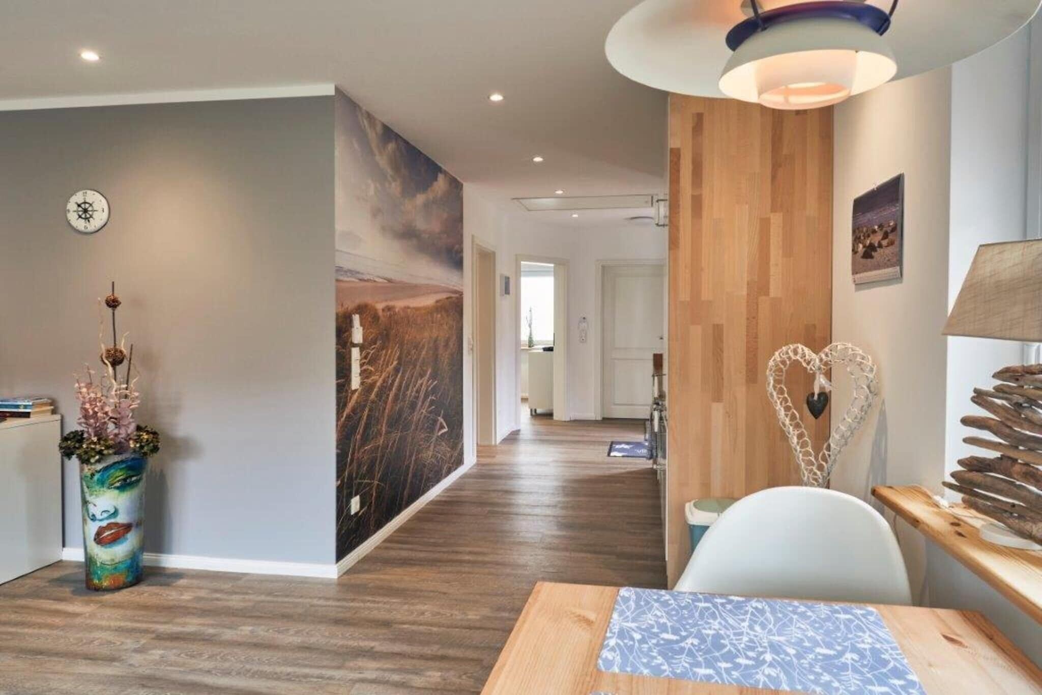 Ein modernes Interieur mit Holzboden, einem Essbereich mit Tisch und Stühlen, einer Wand mit einem großen Gemälde und einer Deckenleuchte.