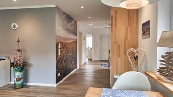 Ein modernes Interieur mit Holzboden, einem Essbereich mit Tisch und Stühlen, einer Wand mit einem großen Gemälde und einer Deckenleuchte.