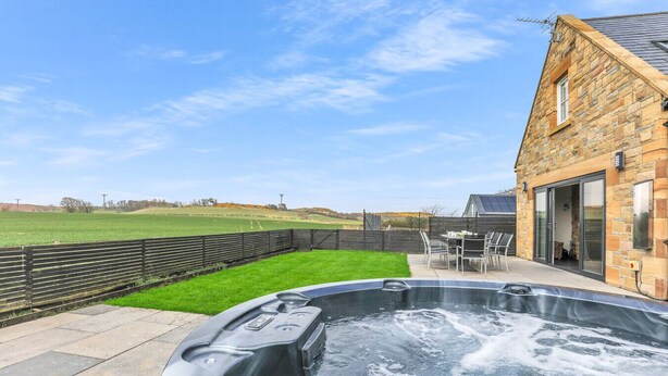 A hot tub in a backyard with a stone building and a grassy field in the background.