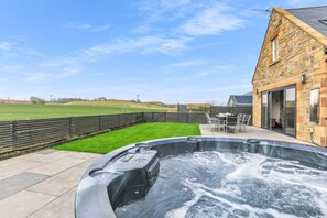 Ein Whirlpool im Garten mit einem Steinhaus und einem grünen Feld im Hintergrund.