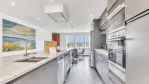 A modern kitchen with stainless steel appliances, a large window, and a painting on the wall.