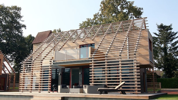 Ein modernes Haus mit einer durchgehenden Holzfassade, großen Glasfenstern und einer Terrasse mit Gartenmöbeln.