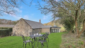 A stone building with a small attached structure, a grassy lawn, and a table with chairs.