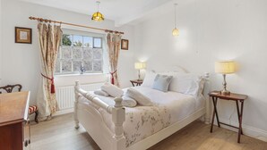A bedroom with a large bed, two bedside tables with lamps, a window with curtains, and a radiator.