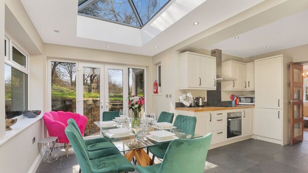 A modern kitchen with white cabinets, a dining area with a glass table and green chairs, and a skylight above the dining area.