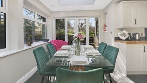 A modern dining room with a glass table, green chairs, and a skylight.