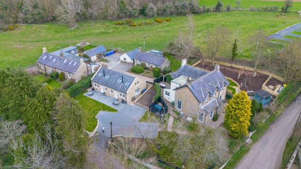 An aerial view of a residential area with multiple houses, a clear road, and surrounding fields.