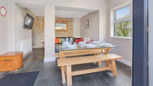 A dining area with a glass table set for four, a wooden bench, and a stone wall in the background.